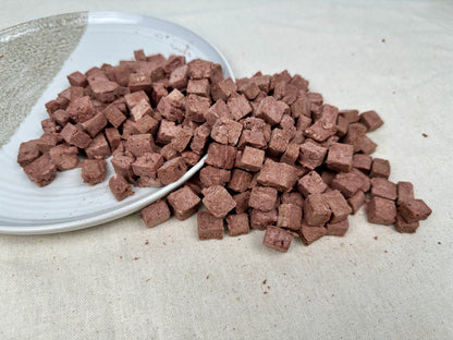 Pile of freeze-dried kangaroo cubes on a ceramic plate, showing their light, airy texture and uniform shape.
