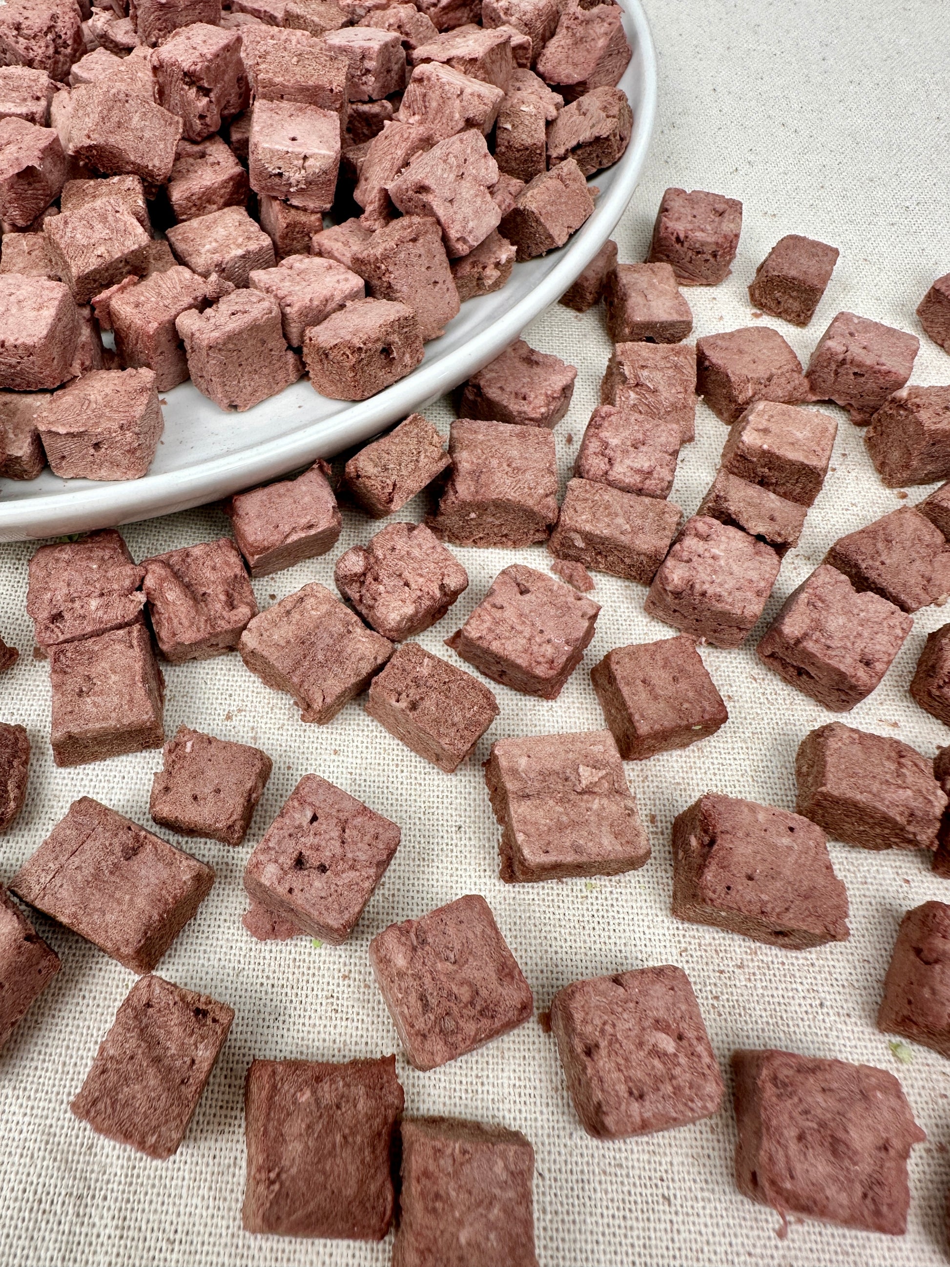 Freeze-dried kangaroo dog treats cut into small cube pieces, displayed in a bowl and spread across fabric.