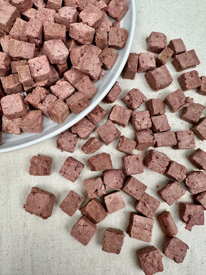 Close-up of freeze-dried kangaroo cubes in a white bowl and scattered on a neutral linen background.